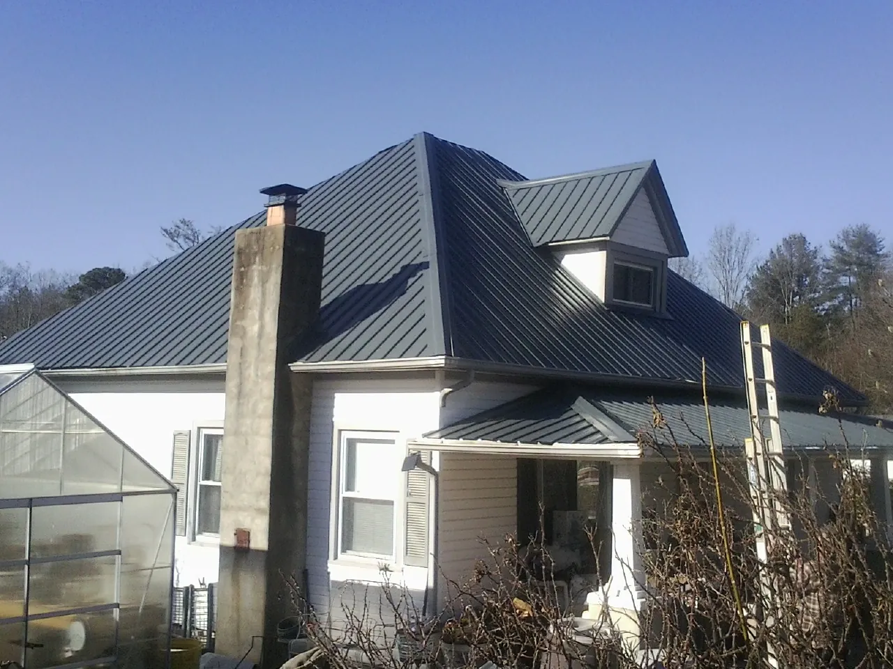 Dark blue standing seam metal roof on a white farmhouse with dormer — Slate & Tile Roof Repair by Roofing Brothers in La Valle