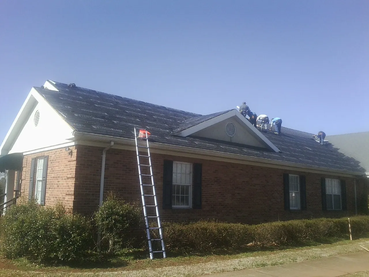 Crew tearing shingles off a brick ranch roof with a ladder set — Emergency Roof Repair work by our crew in La Valle
