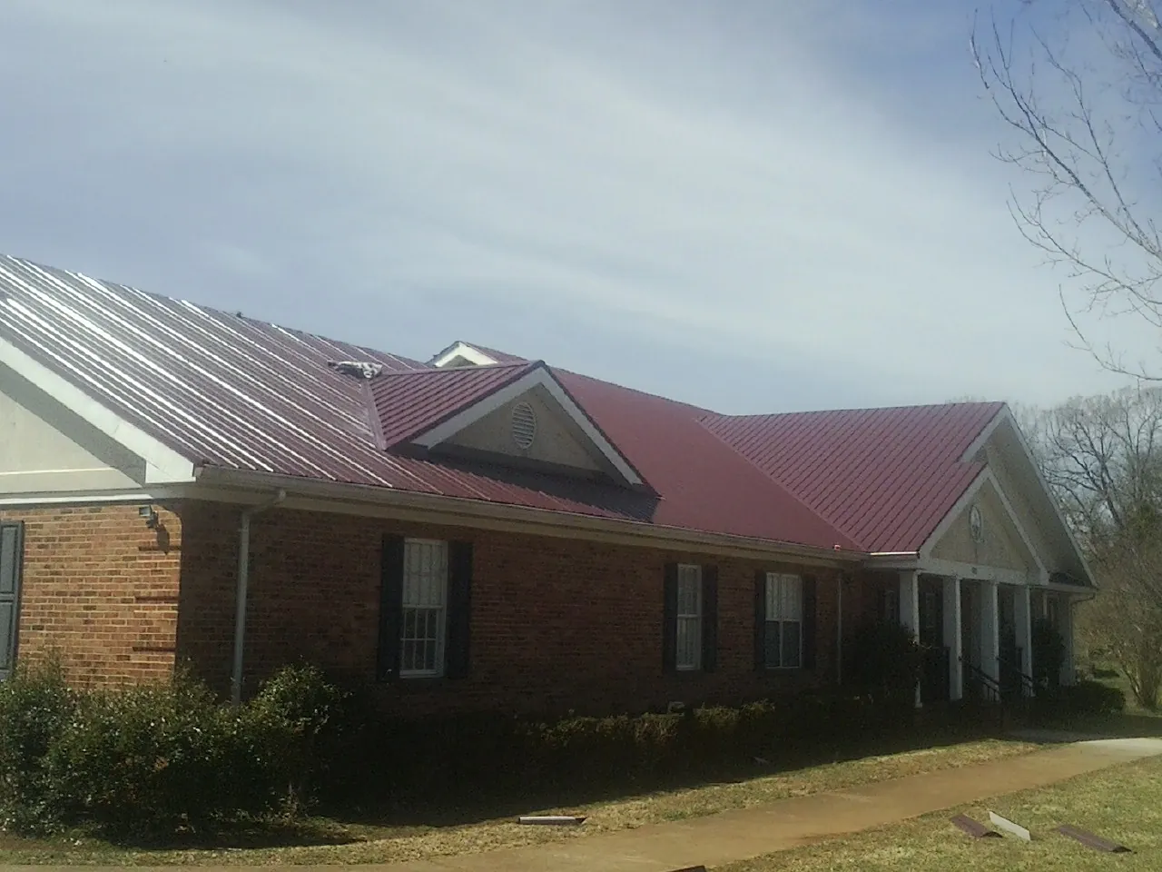Red metal roof with gabled entries on a long brick building, from a Hail Damage Roof Repair job in La Valle