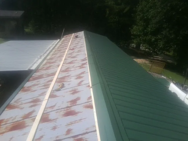 Old rusted panels beside newly installed green metal roofing — Wind Damage Roof Repair by Roofing Brothers in La Valle