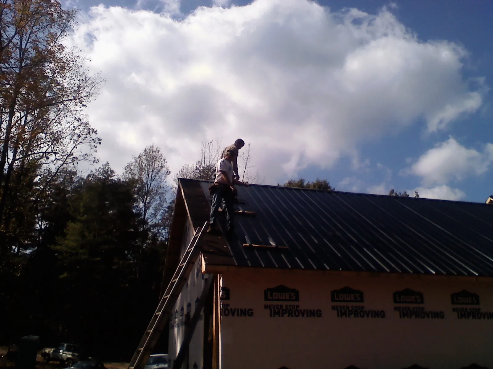 Roofer fastening dark metal panels high against a cloudy sky, from a Roof Inspection job in La Valle