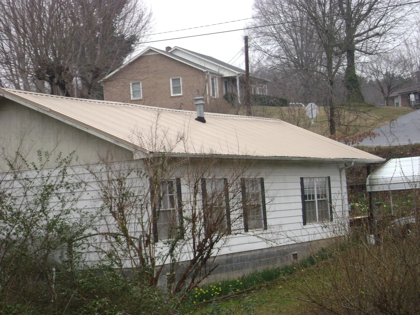 Tan metal roof on a white sided house set into a hillside — Commercial Roofing by Roofing Brothers in La Valle